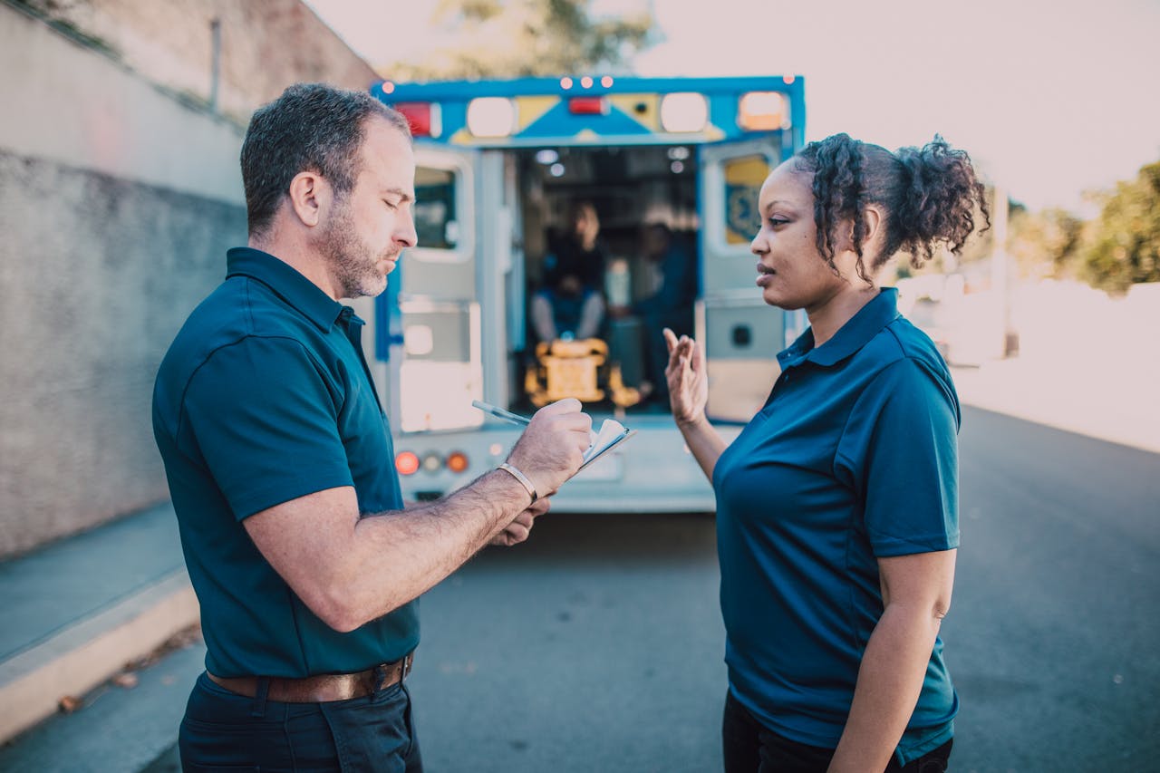 Paramedics conversing and taking notes in front of an ambulance during the day.